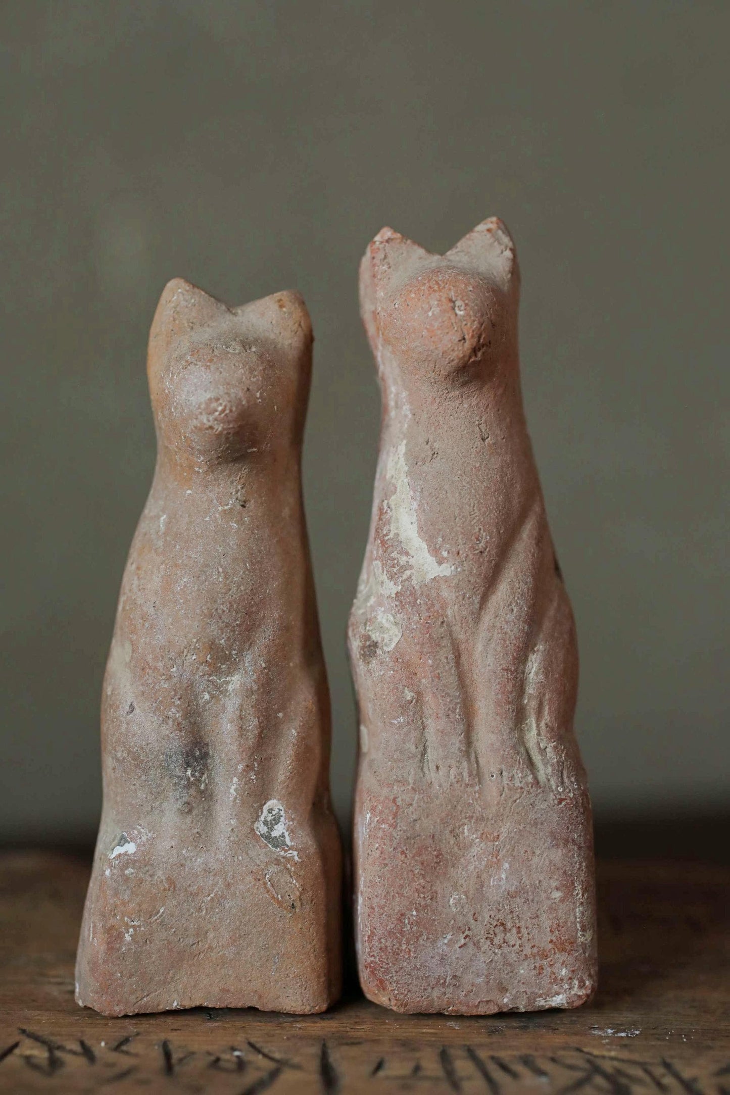 Two ancient clay cat statues, one standing and one sitting, are displayed against a gray background.