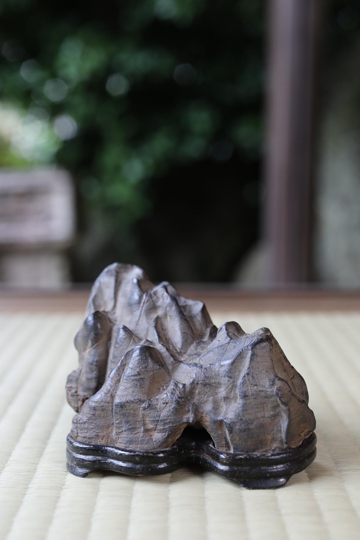 A close-up image of a stone or rock formation, possibly a bonsai tree, placed on a wooden stand or base.