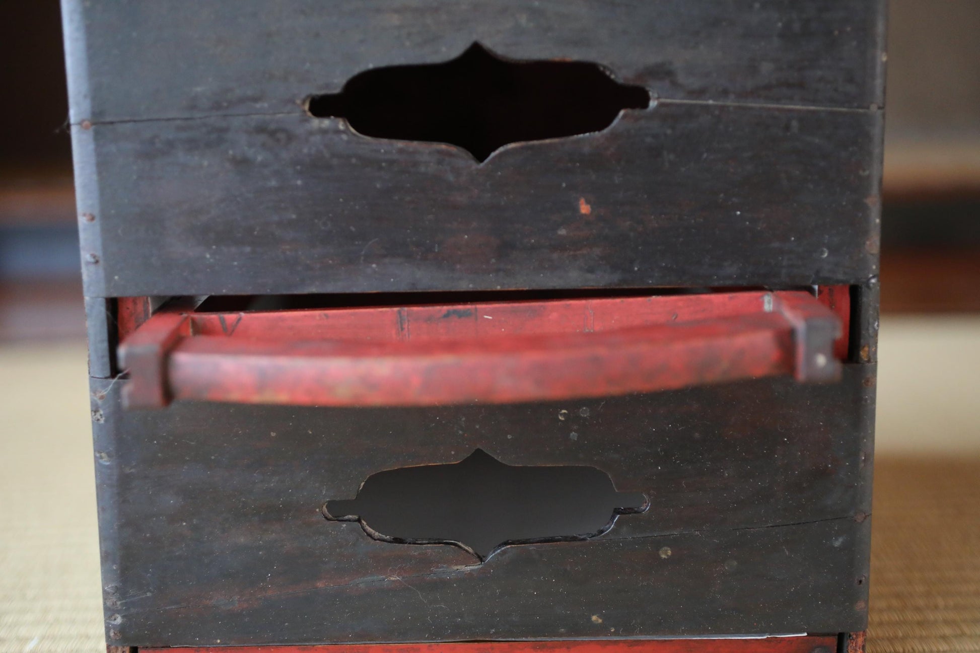 a close-up view of a wooden box with a red handle, featuring a carved design on the front.