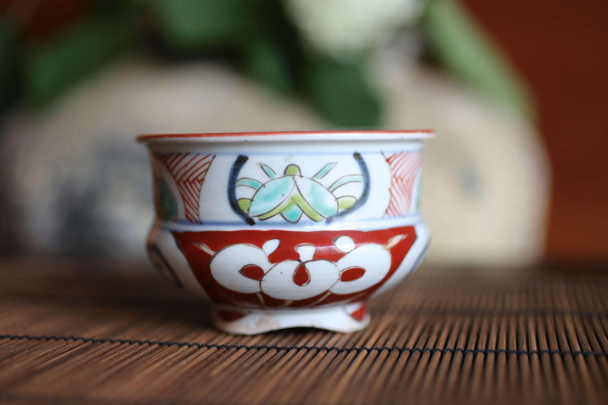 A decorative ceramic bowl with a floral pattern and a red rim sits on a bamboo mat.