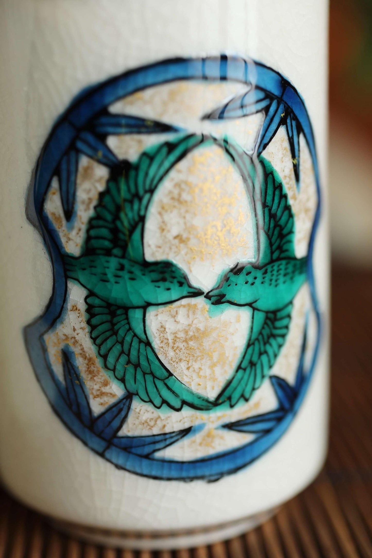 A close-up image of a ceramic mug or container with a decorative design featuring two green birds in a circular pattern.