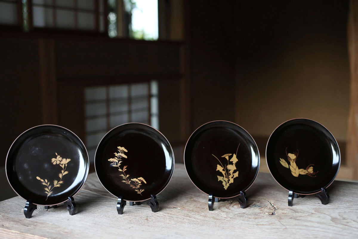 A collection of four black plates with gold floral designs, each placed on a stand on a wooden surface.