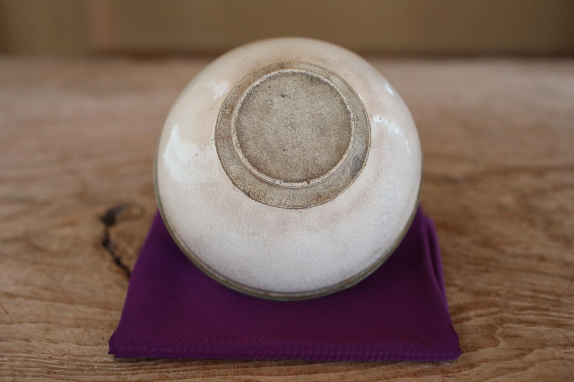A white ceramic bowl with a circular design sits on a purple cloth on a wooden surface.