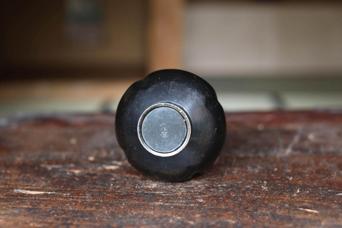 A black, round object with a silver circular emblem on it, sitting on a wooden surface.