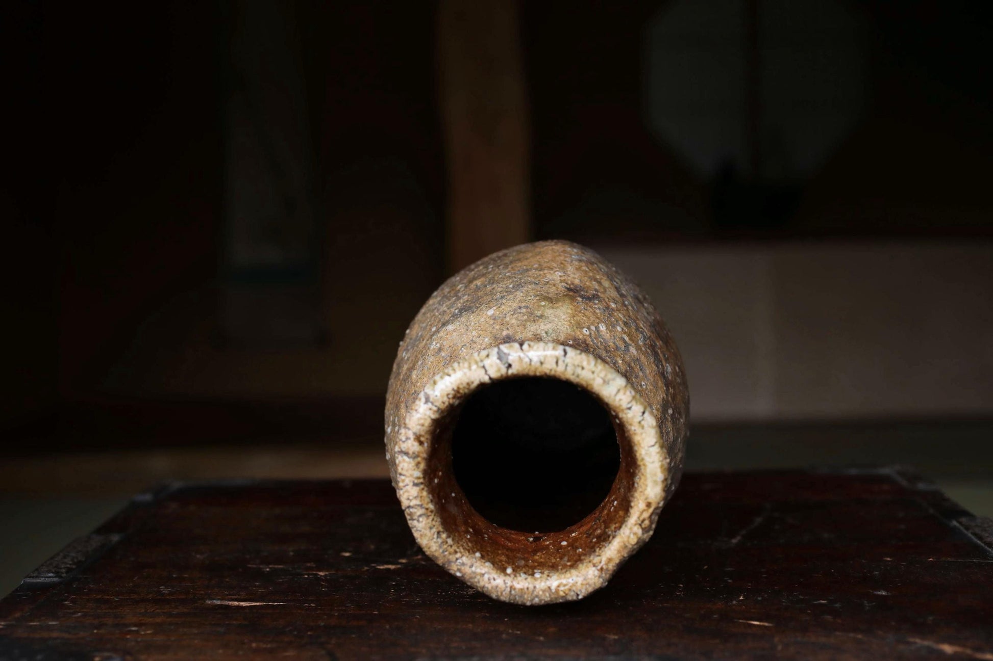 A weathered, rusted vase with a large hole in the center sits on a wooden surface, with a blurred background.