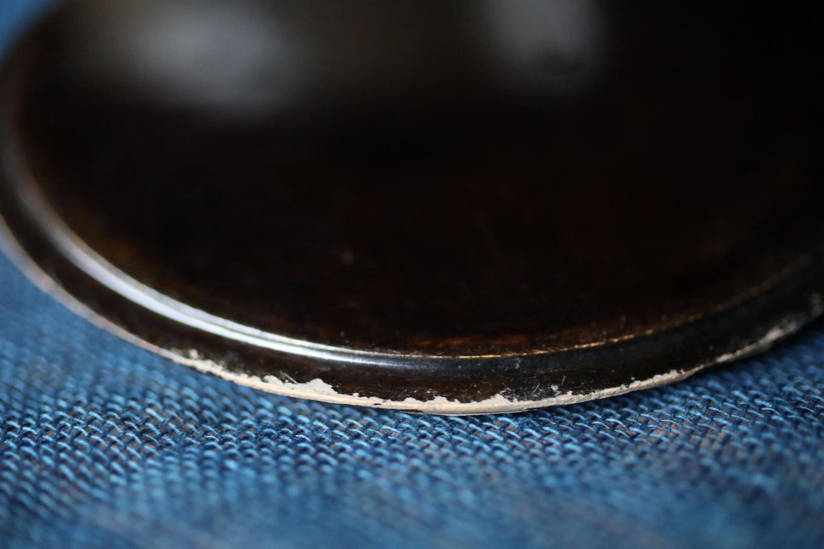 A close-up view of a dark, shiny surface, possibly a metal or ceramic object, resting on a blue textured surface.