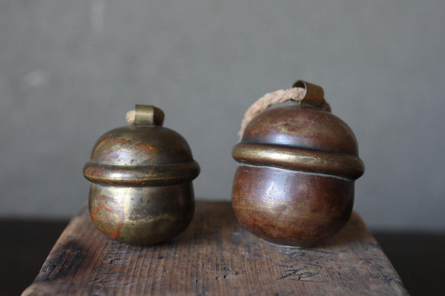Two antique brass bells with rusted surfaces are placed on a wooden surface against a gray background.