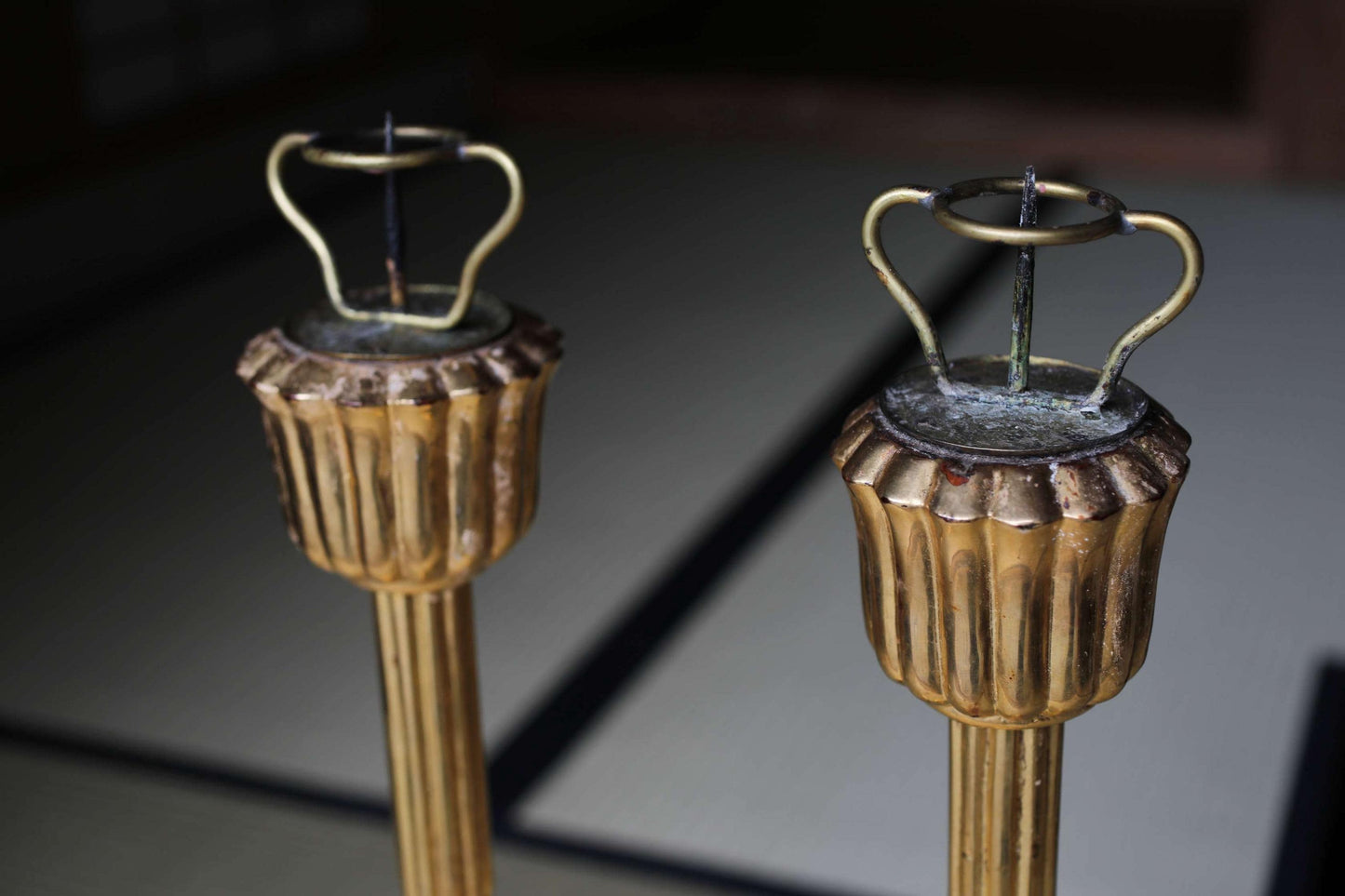 two ornate golden candlesticks with a curved top, standing side by side on a dark surface.