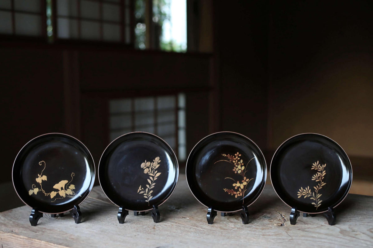 A collection of four black plates with gold floral designs, each placed on a stand on a wooden surface.
