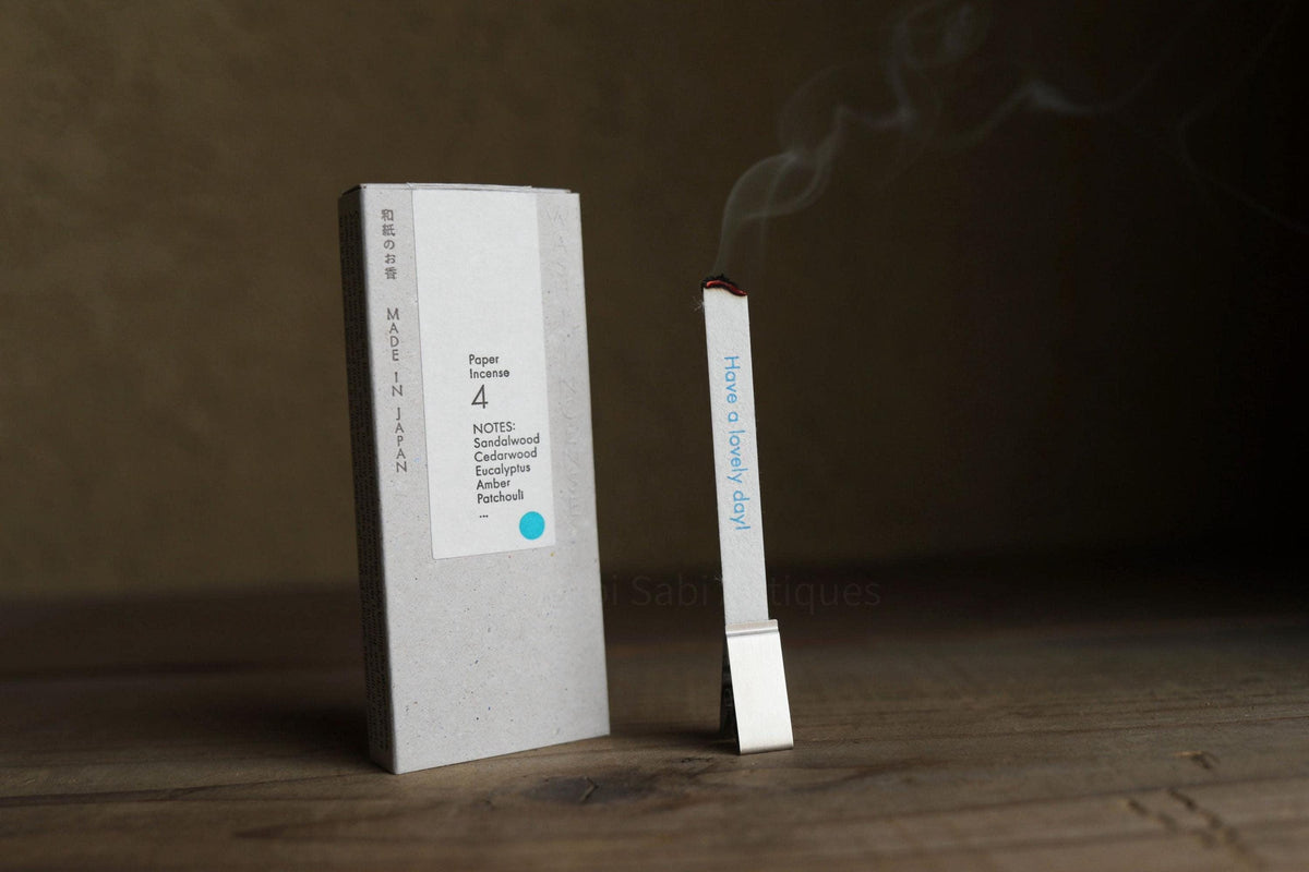 a white box with text on it, standing next to a small white stick with smoke coming out of it, placed on a wooden surface.