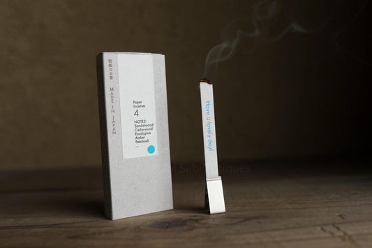 a white box with text on it, standing next to a small white stick with smoke coming out of it, placed on a wooden surface.