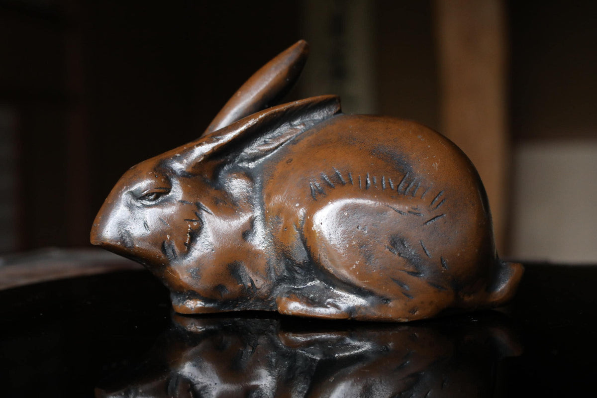 A bronze sculpture of a rabbit sitting on a reflective surface.