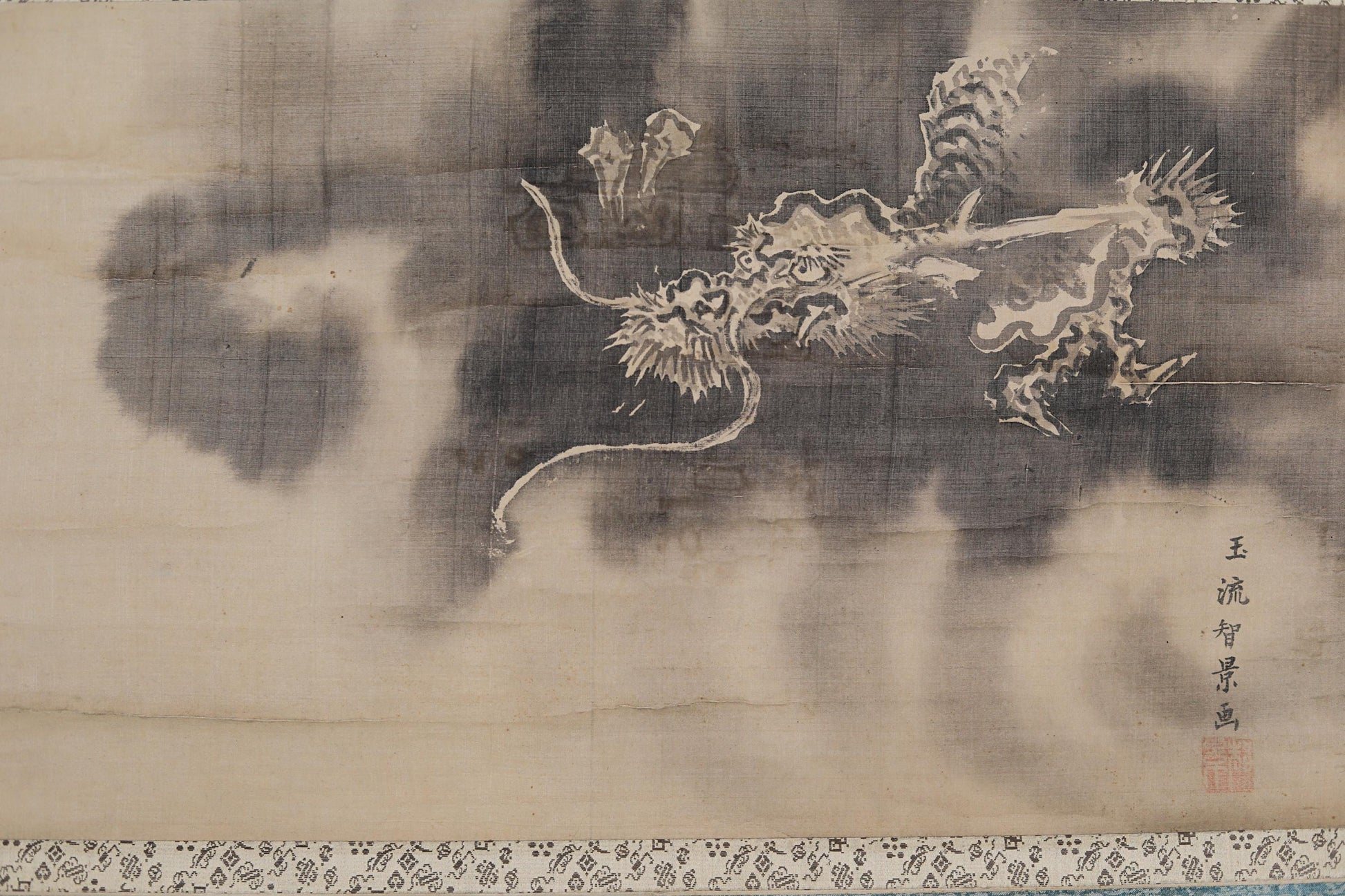 以下が含まれることがあります： 飛行する龍を描いた、日本のアンティーク巻物絵。龍は、暗く煙る雲を背景に白で描かれています。巻物には日本語のテキストと赤い印鑑が含まれています。