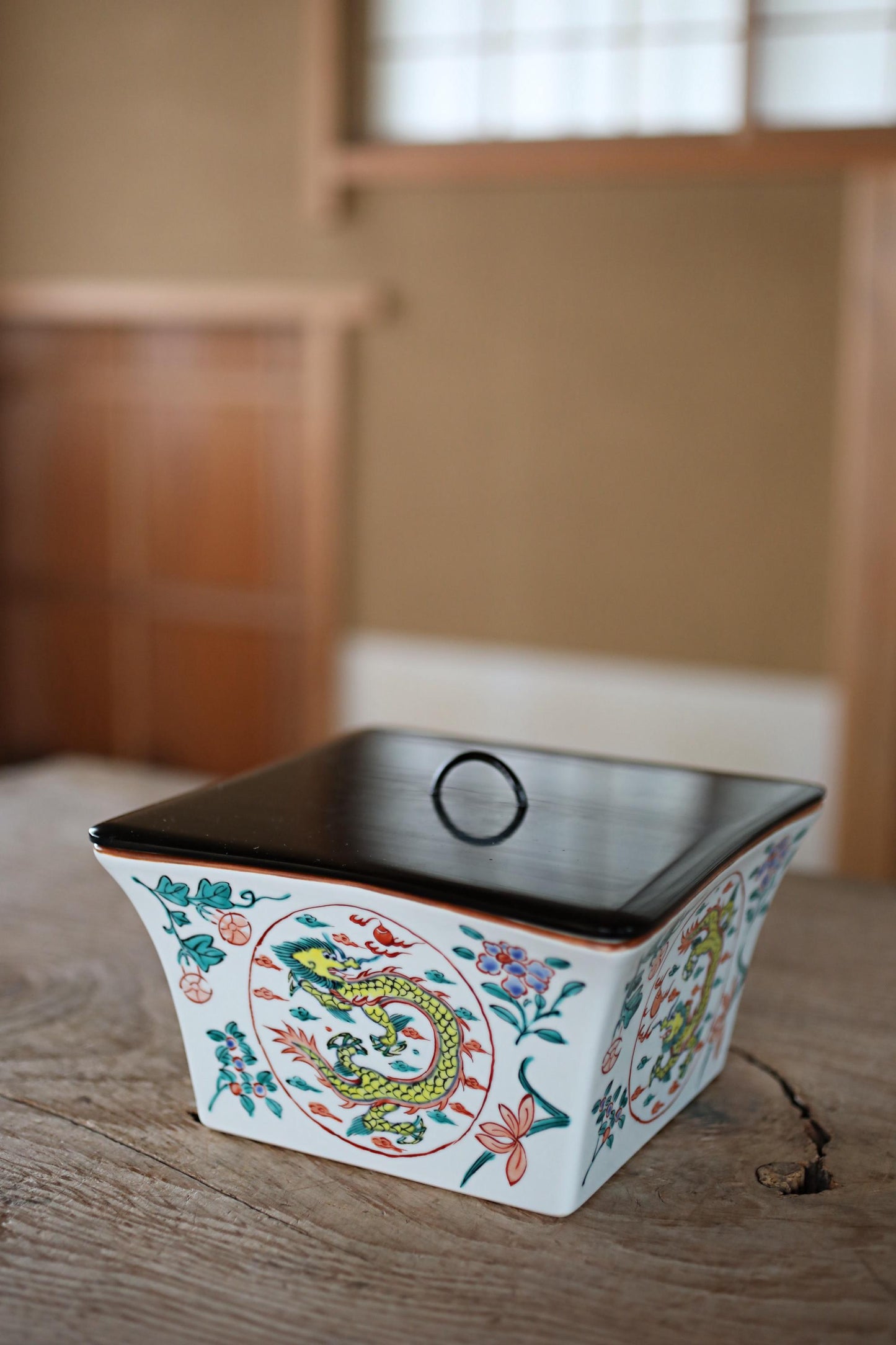 A decorative ceramic container with a dragon design sits on a wooden surface.