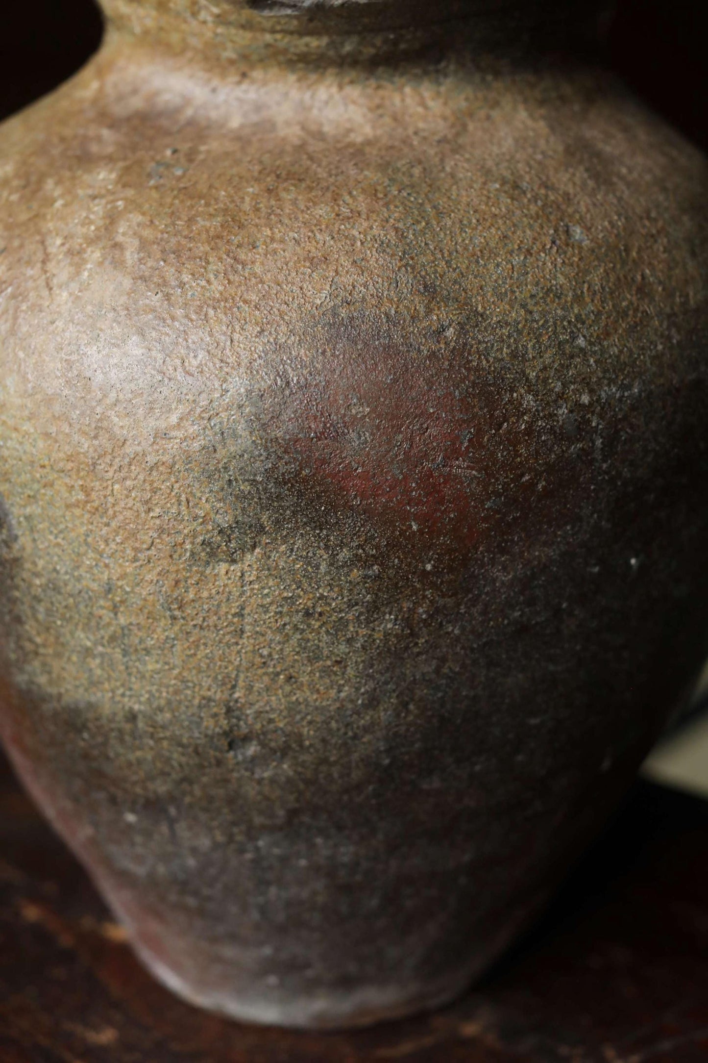 A close-up image of a large, weathered clay vase with a reddish-brown hue and visible cracks and chips on its surface.