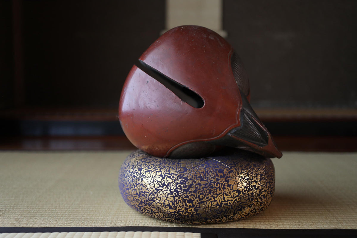 A red ceramic object with a pointed end and a black handle is placed on a blue and gold decorative object, which is sitting on a white mat.