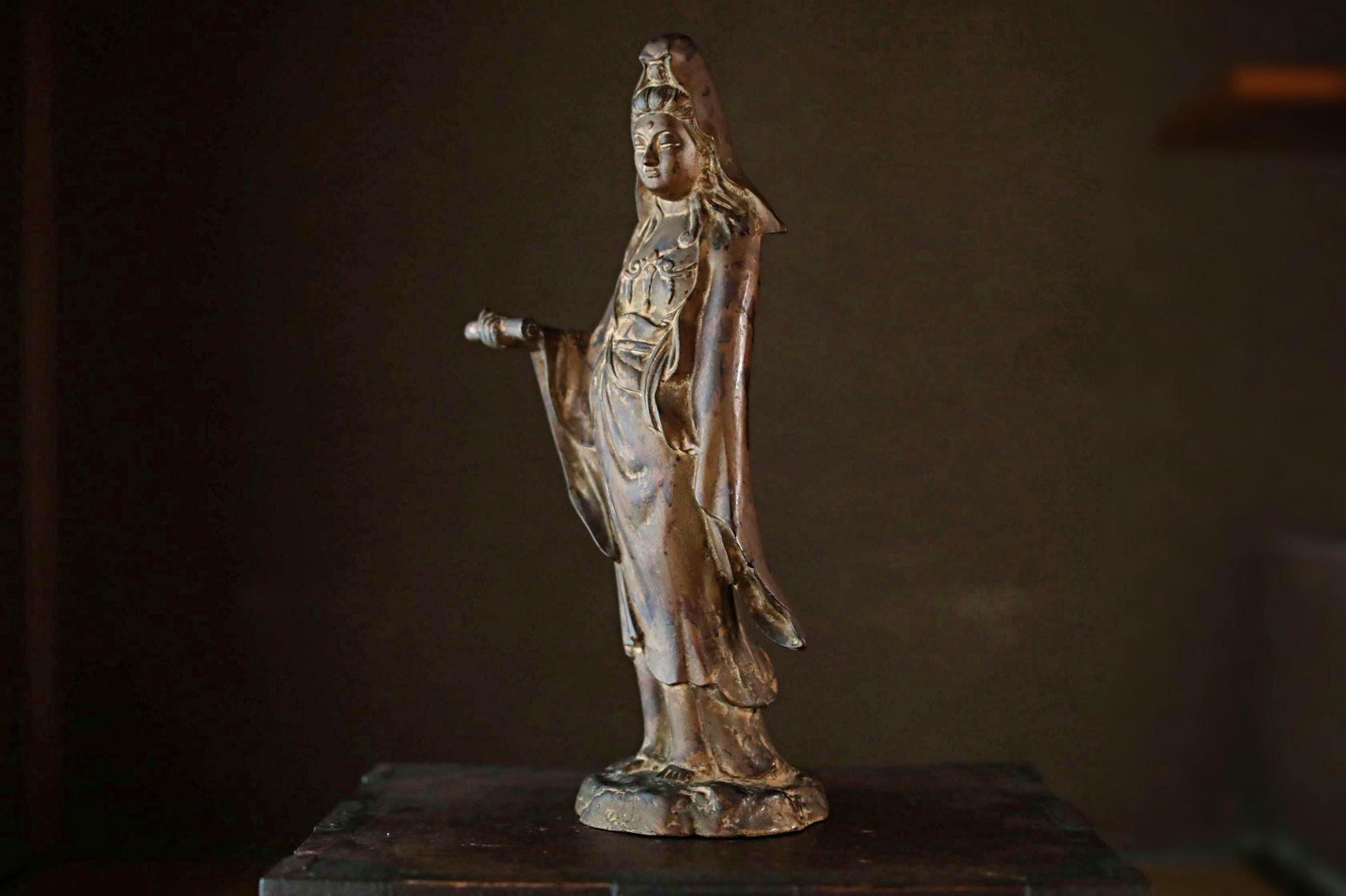 A bronze statue of a woman with a long, flowing robe and a headdress, standing on a wooden surface.