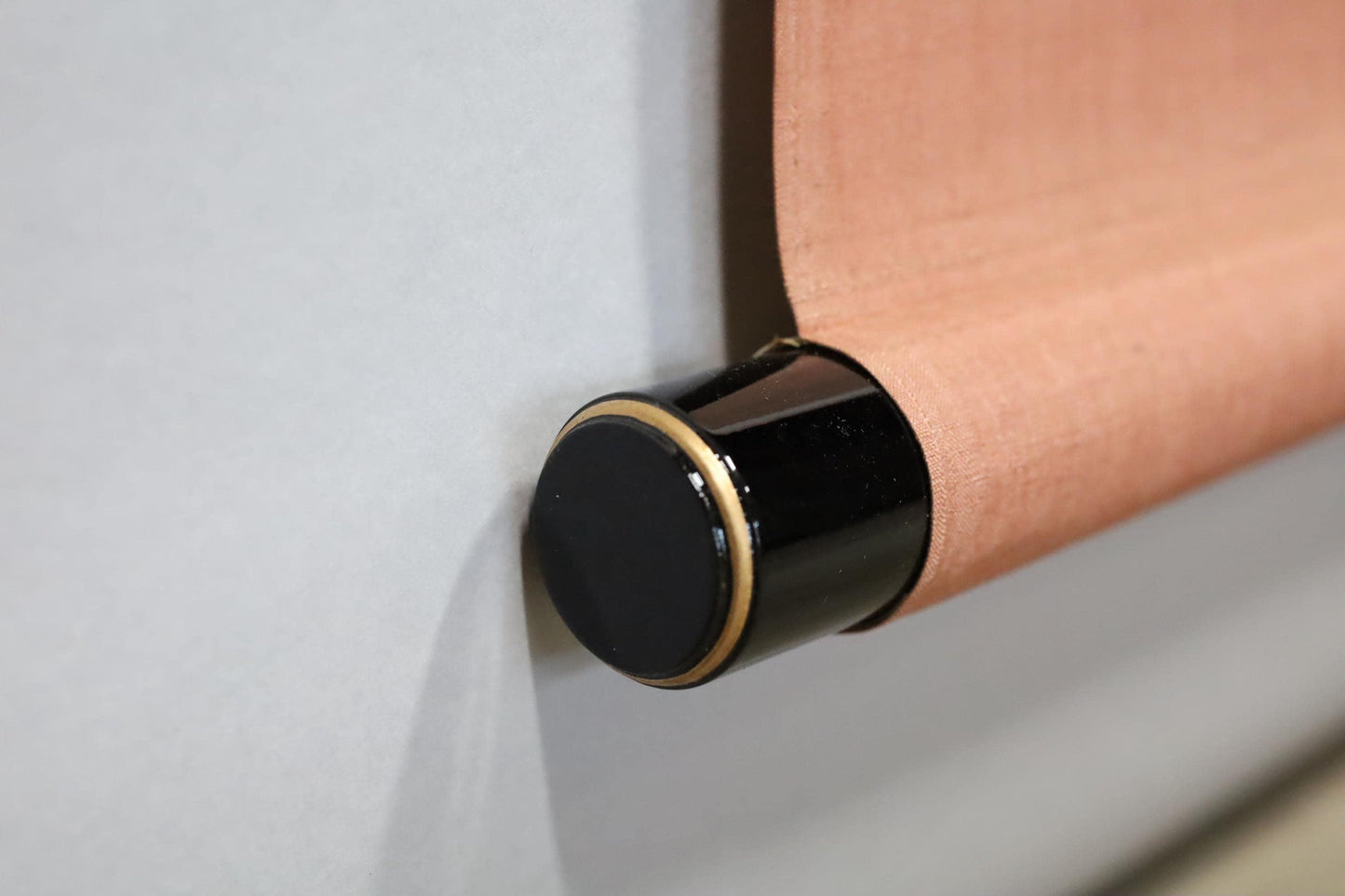 A close-up view of a black and gold roller blind, with a gold-colored roller at the top and a black roller at the bottom.