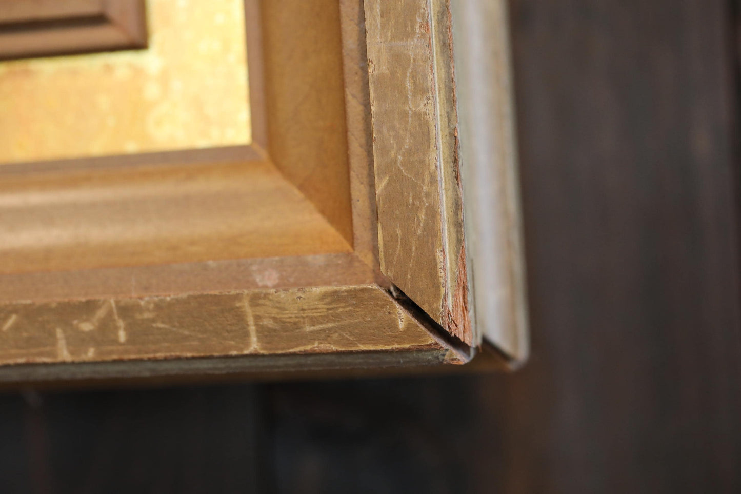 a close-up view of a wooden frame with a gold-colored border, set against a dark background.