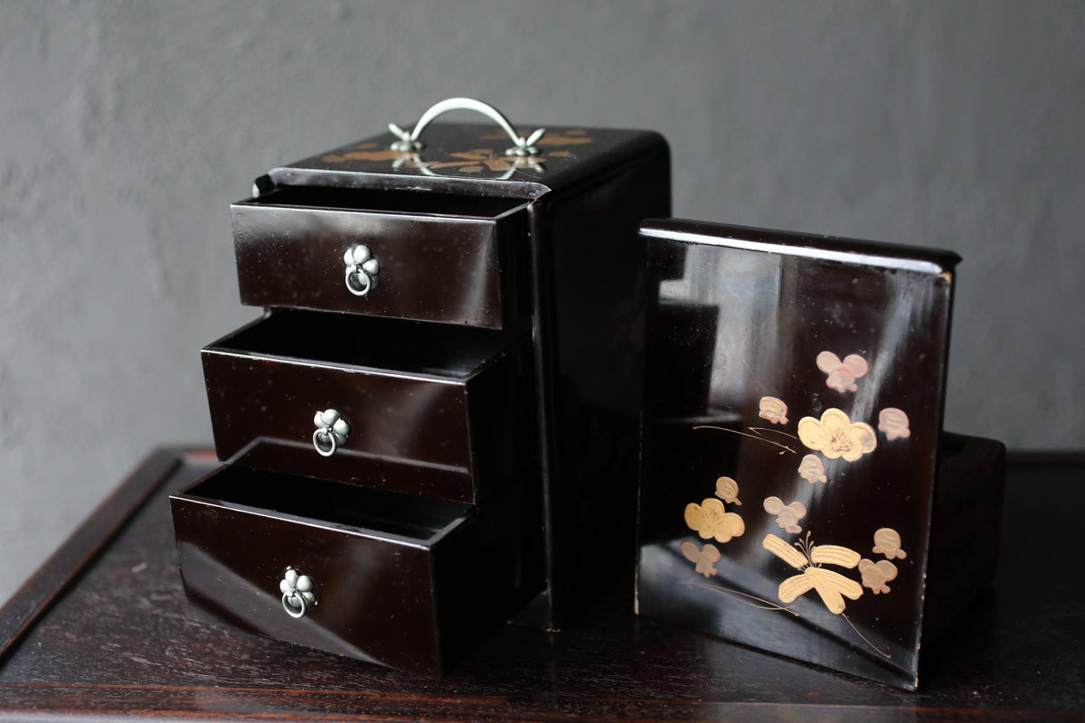 A black wooden box with three drawers and a handle on top, sitting on a dark surface.
