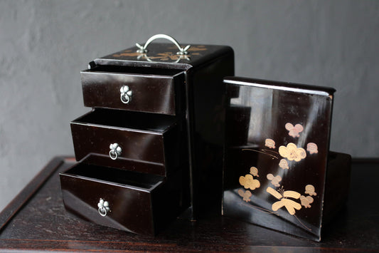 A black wooden box with three drawers and a handle on top, sitting on a dark surface.