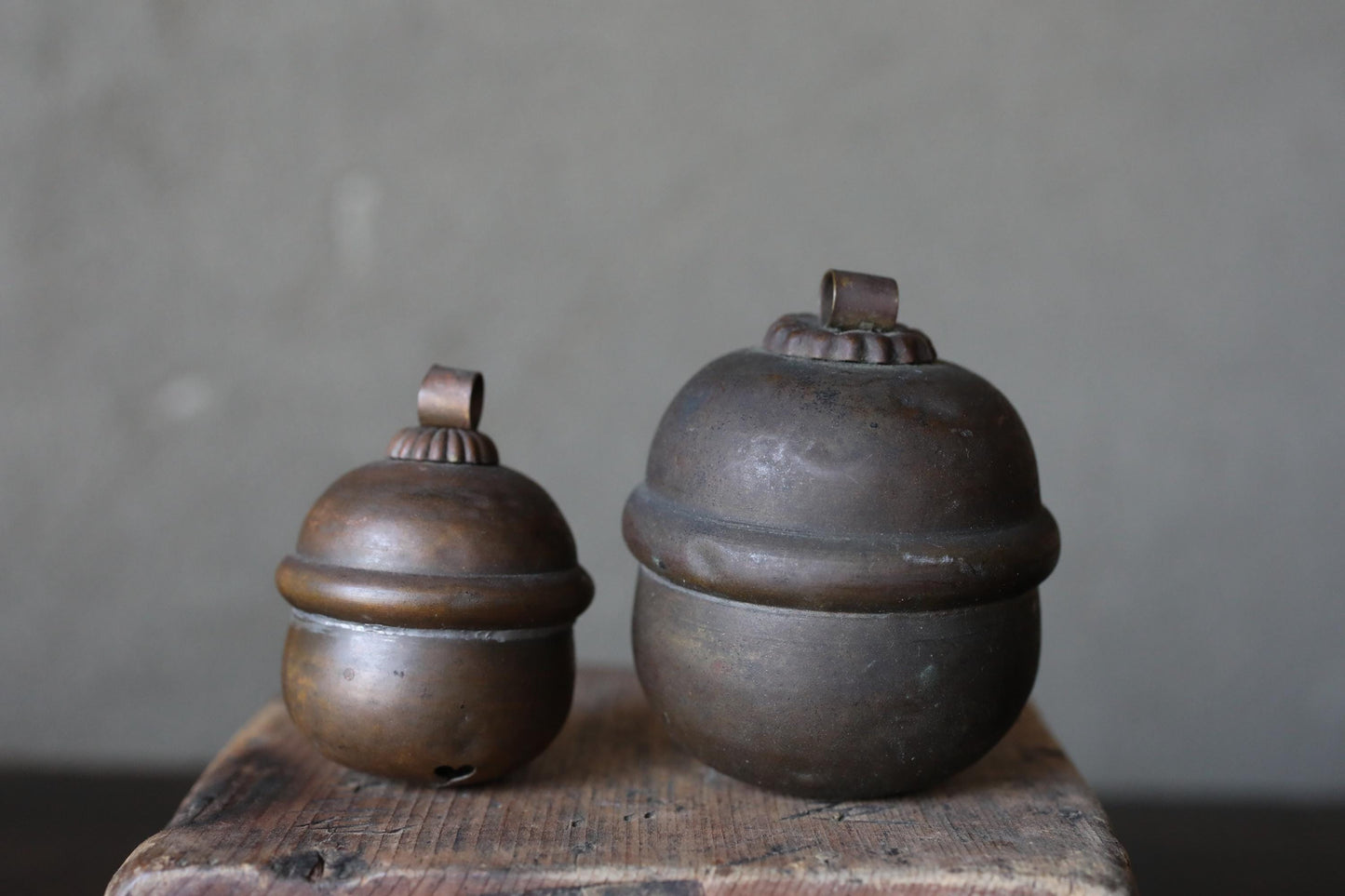 Two antique brass bells are displayed on a wooden surface against a plain background.