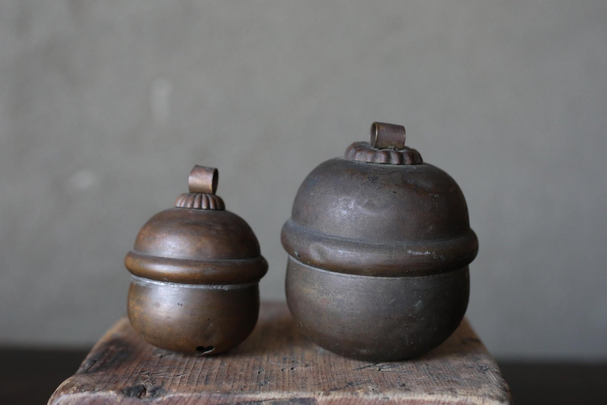 Two antique brass bells are displayed on a wooden surface against a plain background.