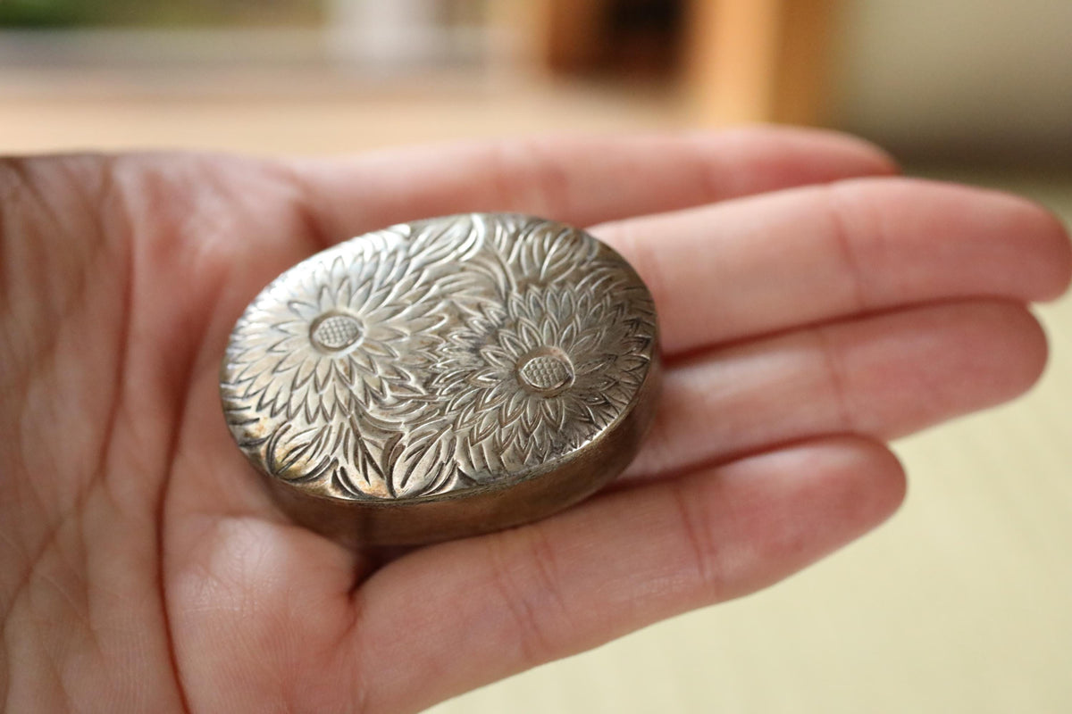 A hand holding a small, ornate metal object with a floral design.