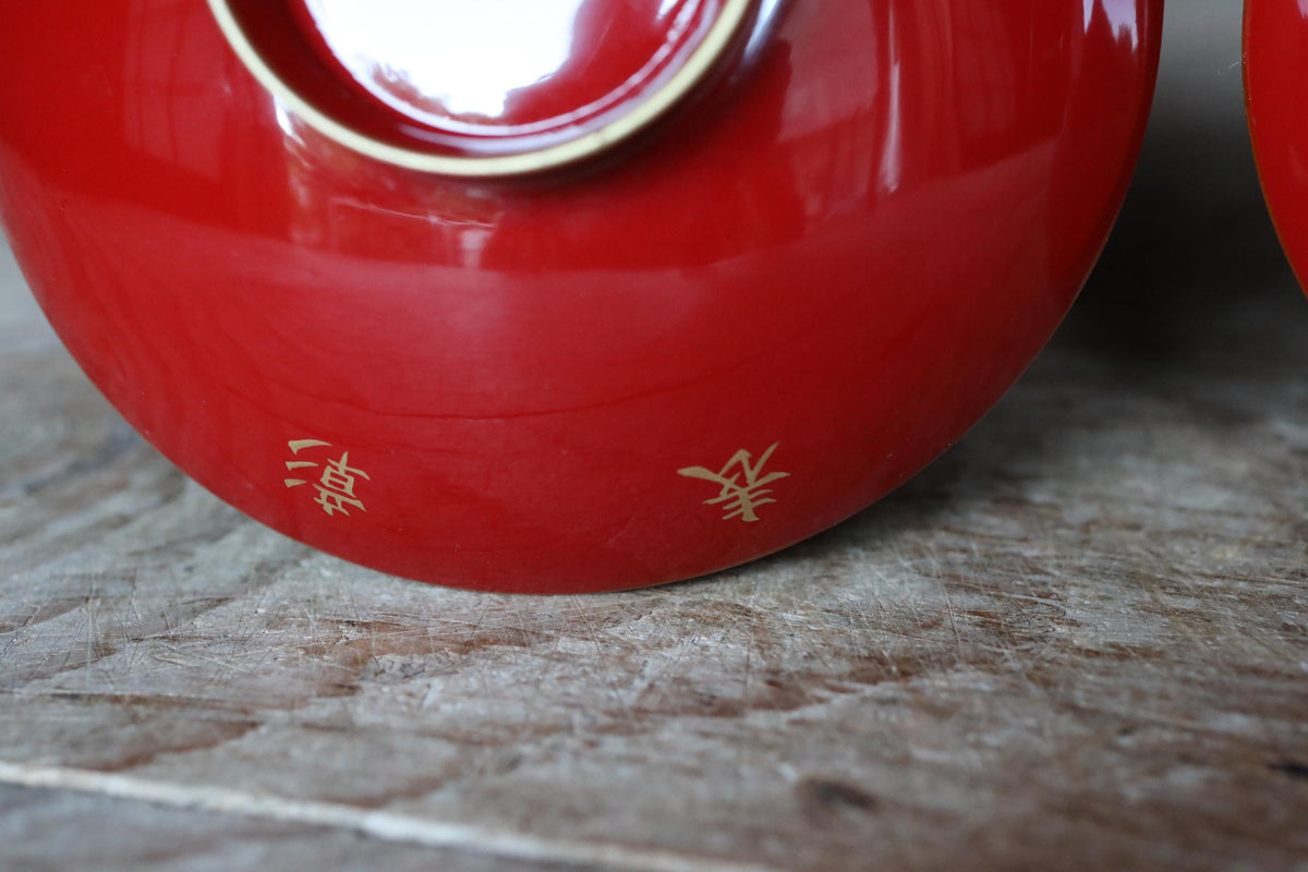 A close-up view of a red ceramic bowl or container with gold Chinese characters on it, placed on a wooden surface.