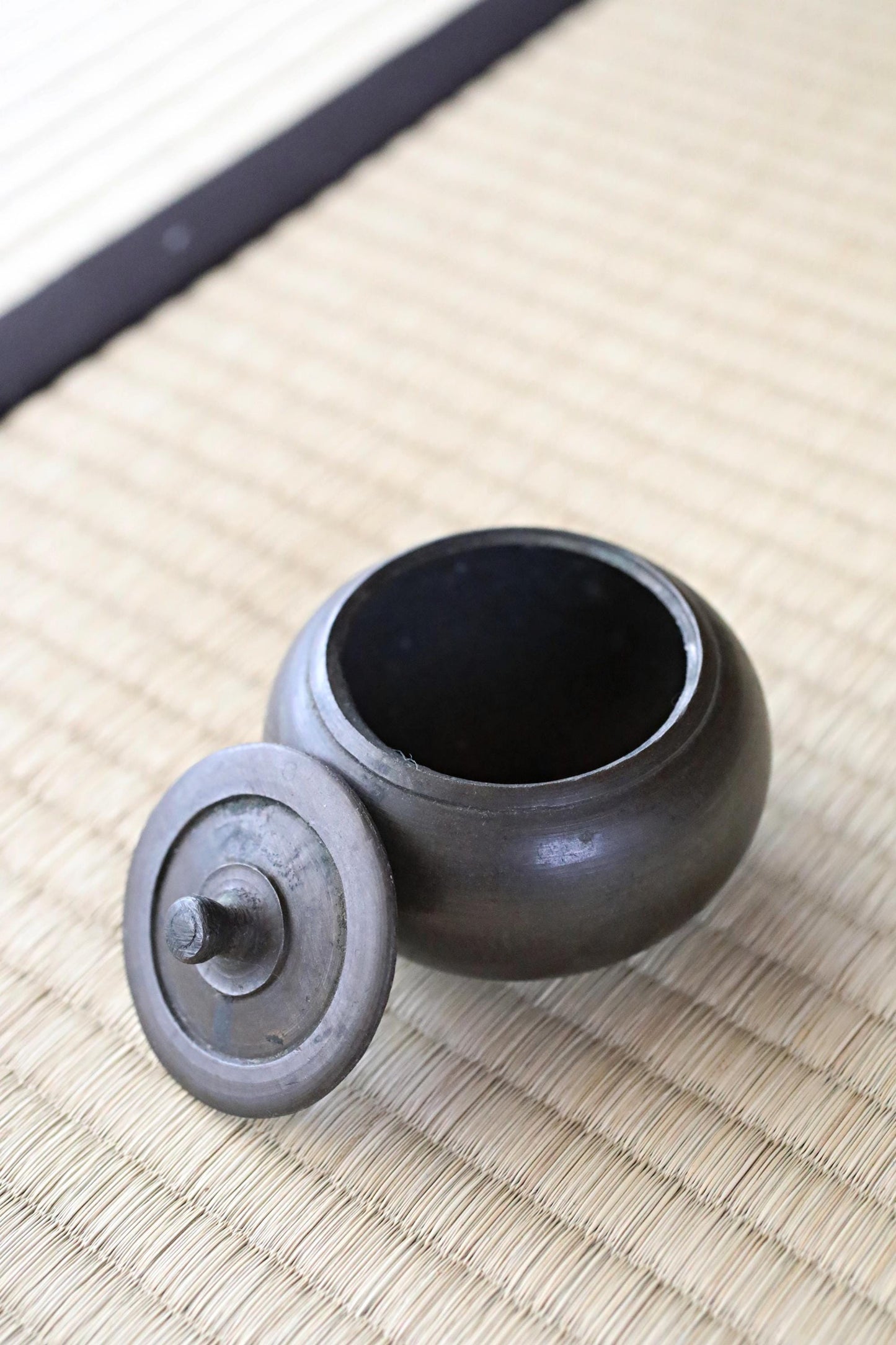 A black metal teapot with a lid sits on a woven mat.