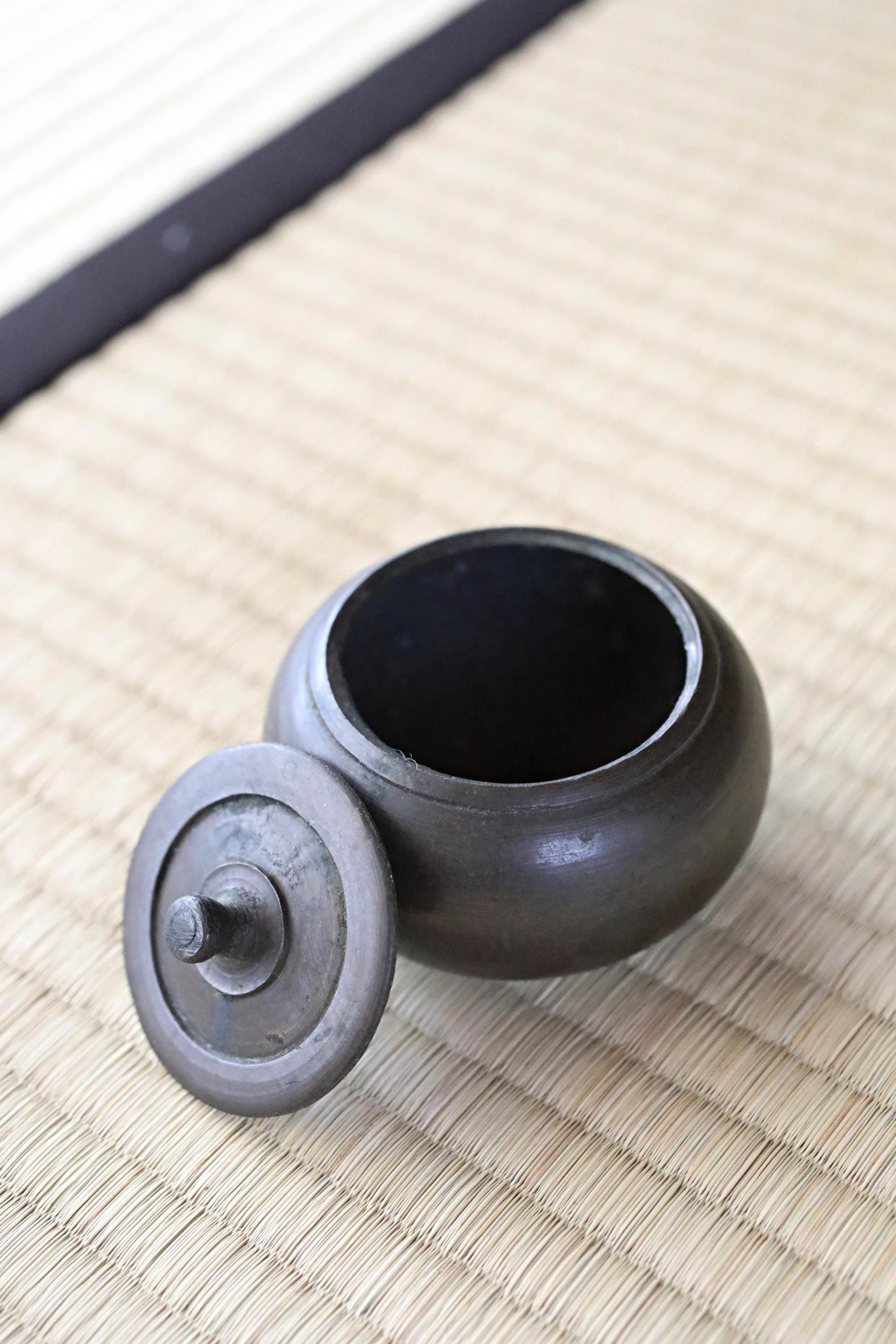A black metal teapot with a lid sits on a woven mat.