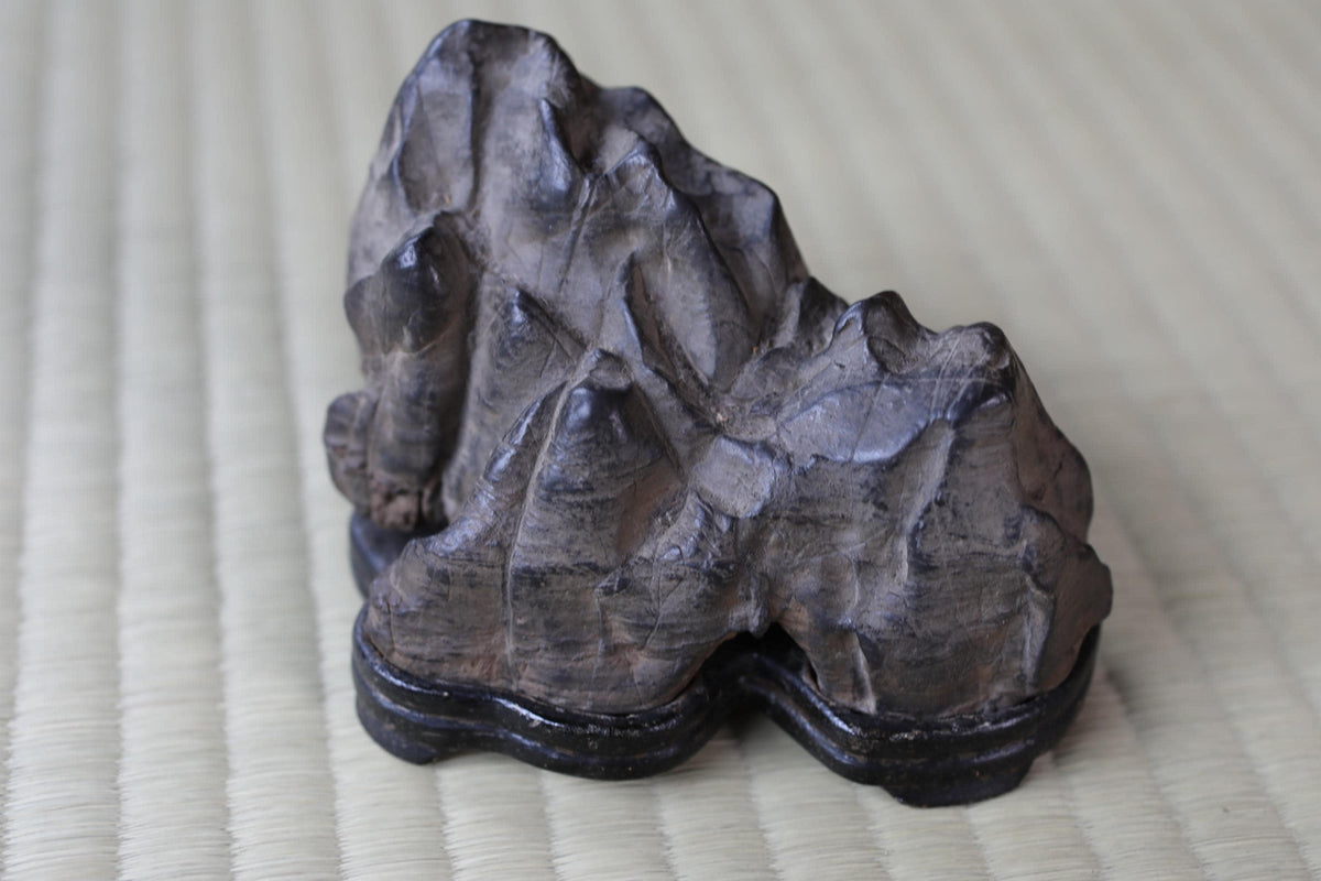 A dark gray rock with jagged edges sits on a black base, placed on a woven mat.