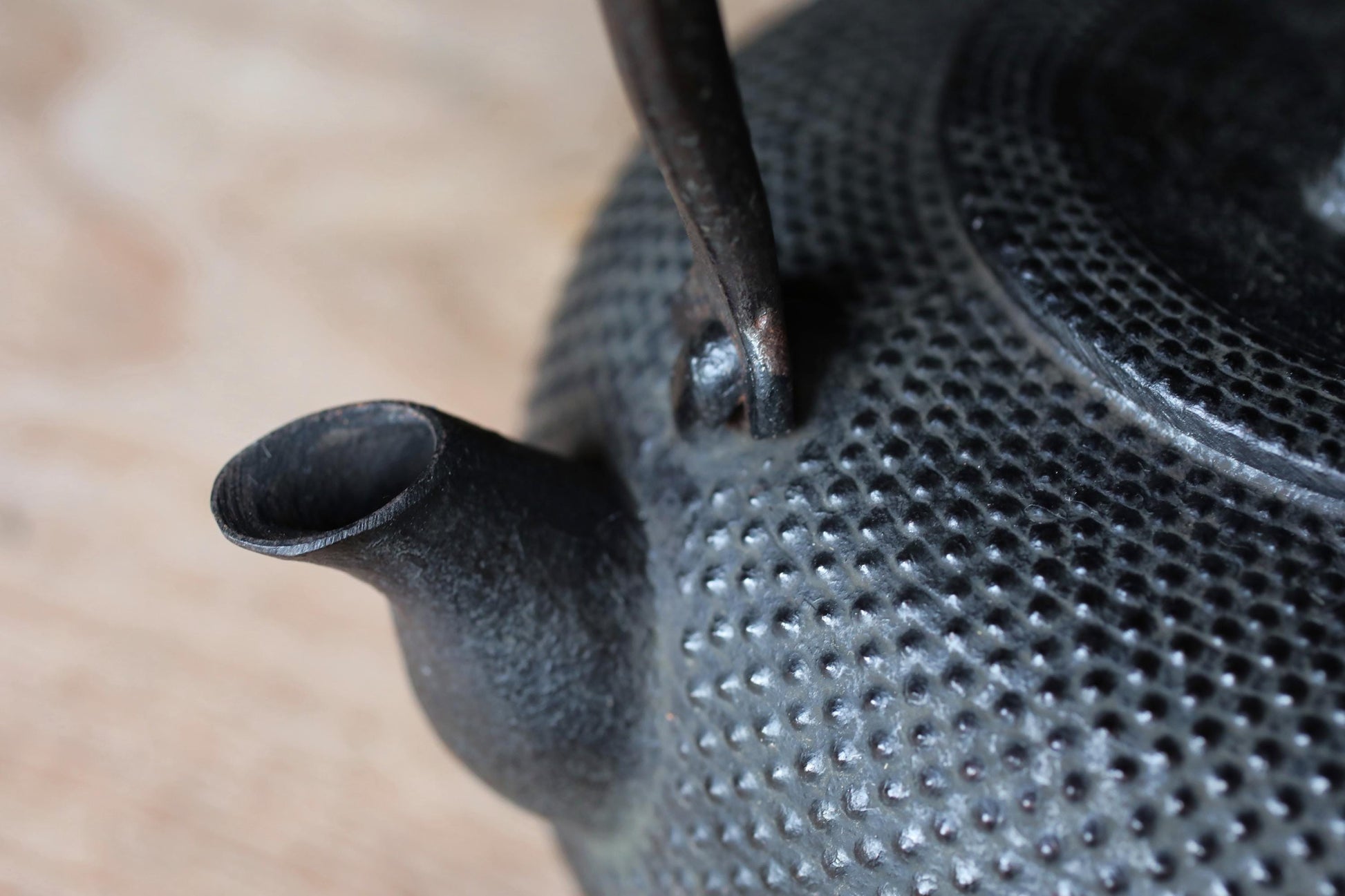 A close-up view of a black metal teapot with a textured surface, featuring a spout and handle.