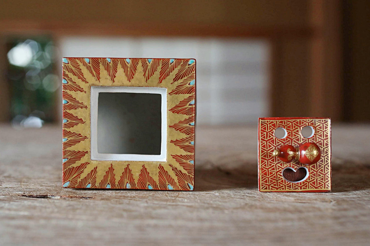 two small, ornate objects with a red and gold color scheme, placed on a wooden surface.
