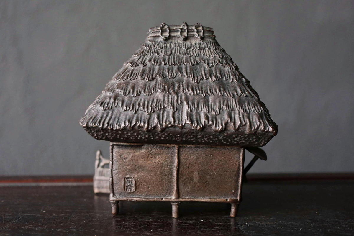 A metal sculpture of a house with a thatched roof, sitting on a dark surface.