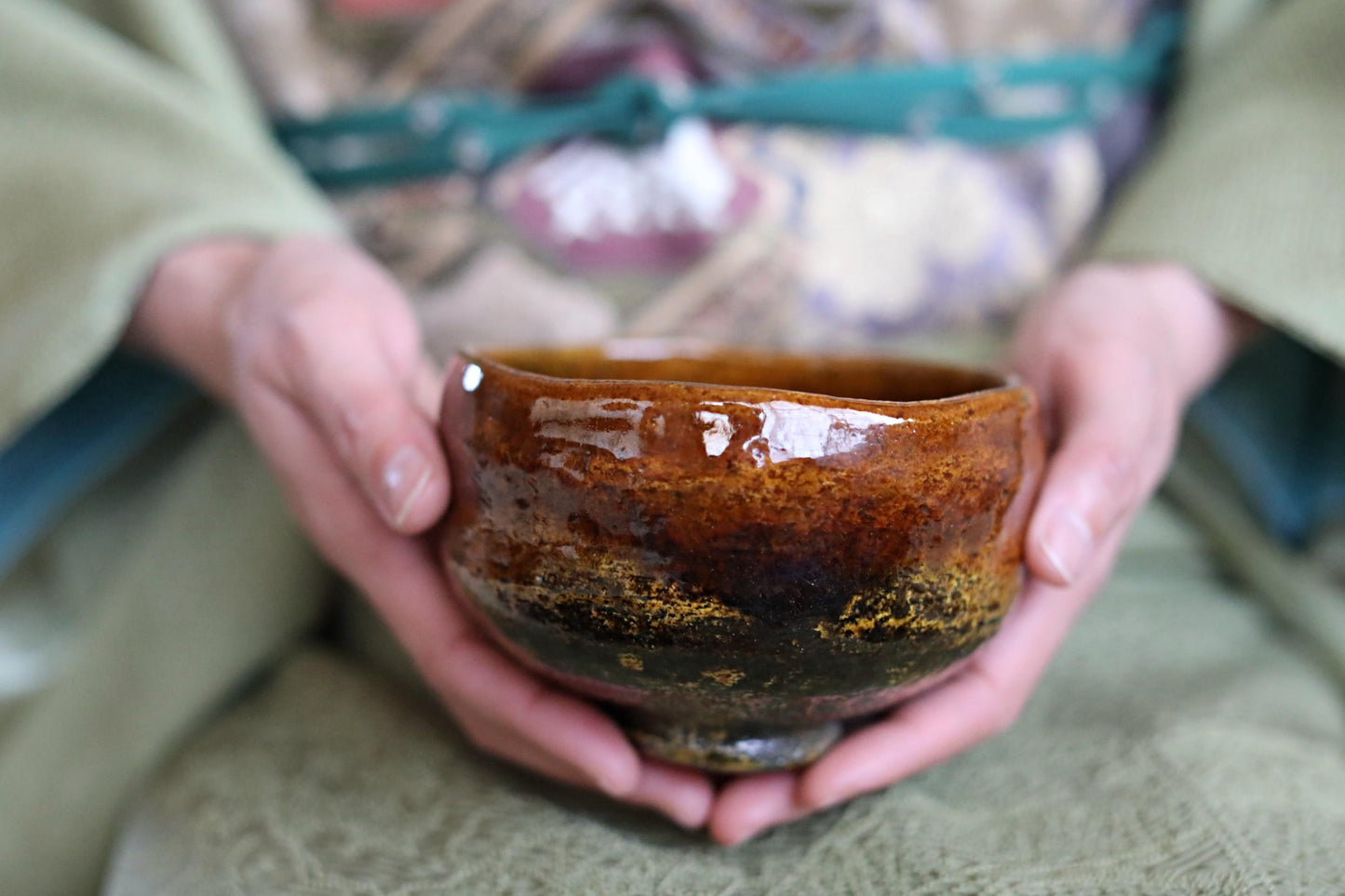 A person's hands holding a brown ceramic bowl with a floral pattern.