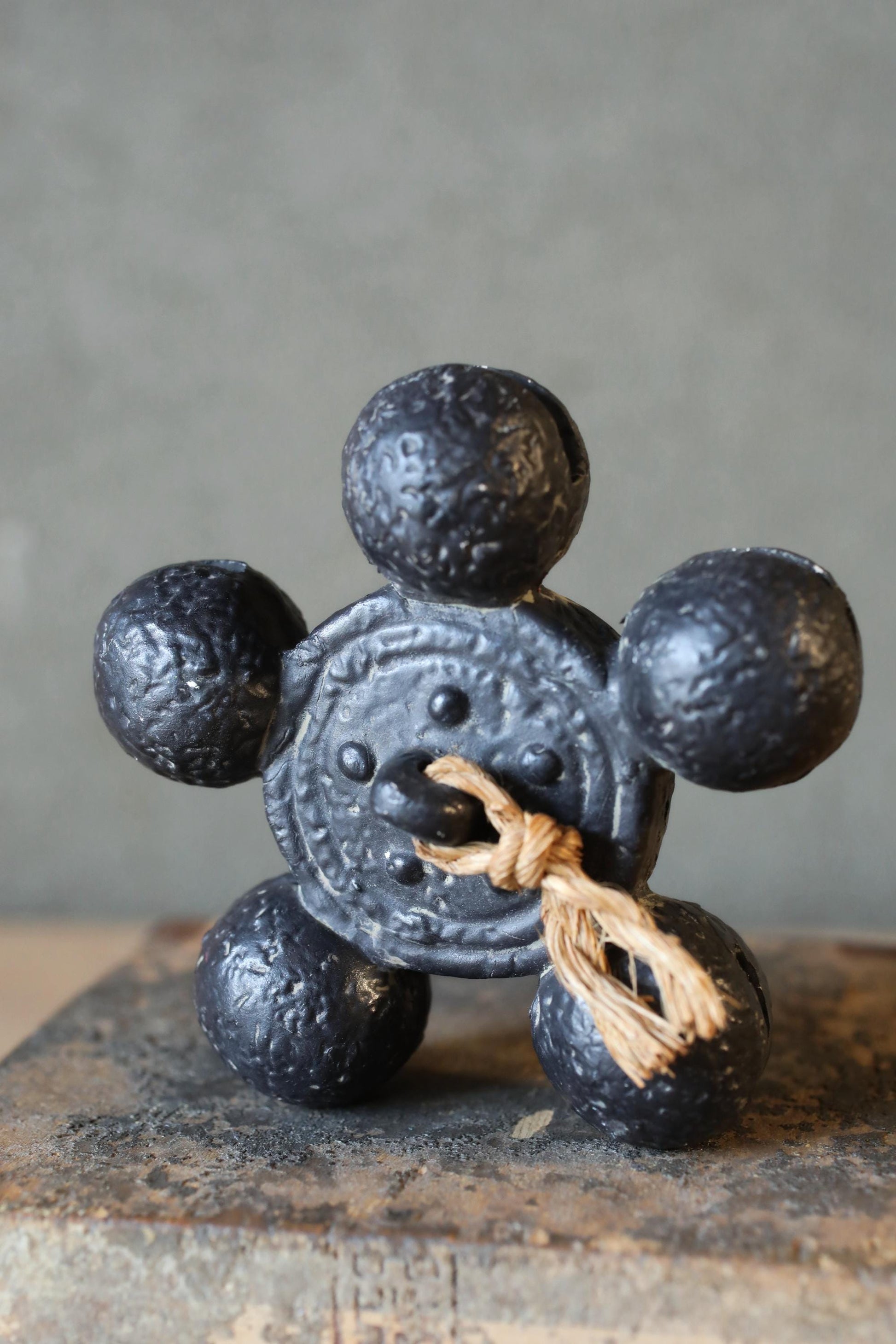 A black metal sculpture with a circular design and a string attached to it, sitting on a wooden surface.