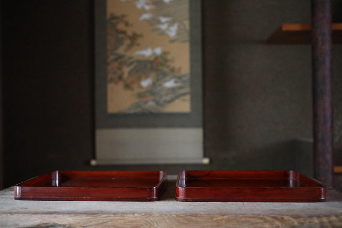 two wooden trays placed on a wooden surface, with a painting or artwork in the background.