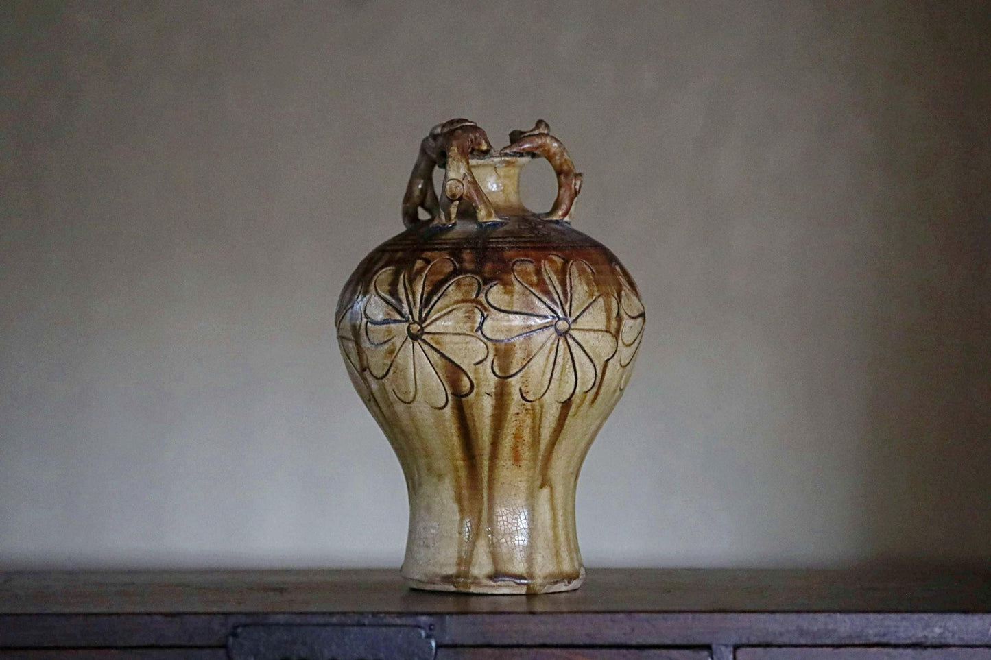 A ceramic vase with a floral design on its surface, placed on a wooden surface against a plain background.