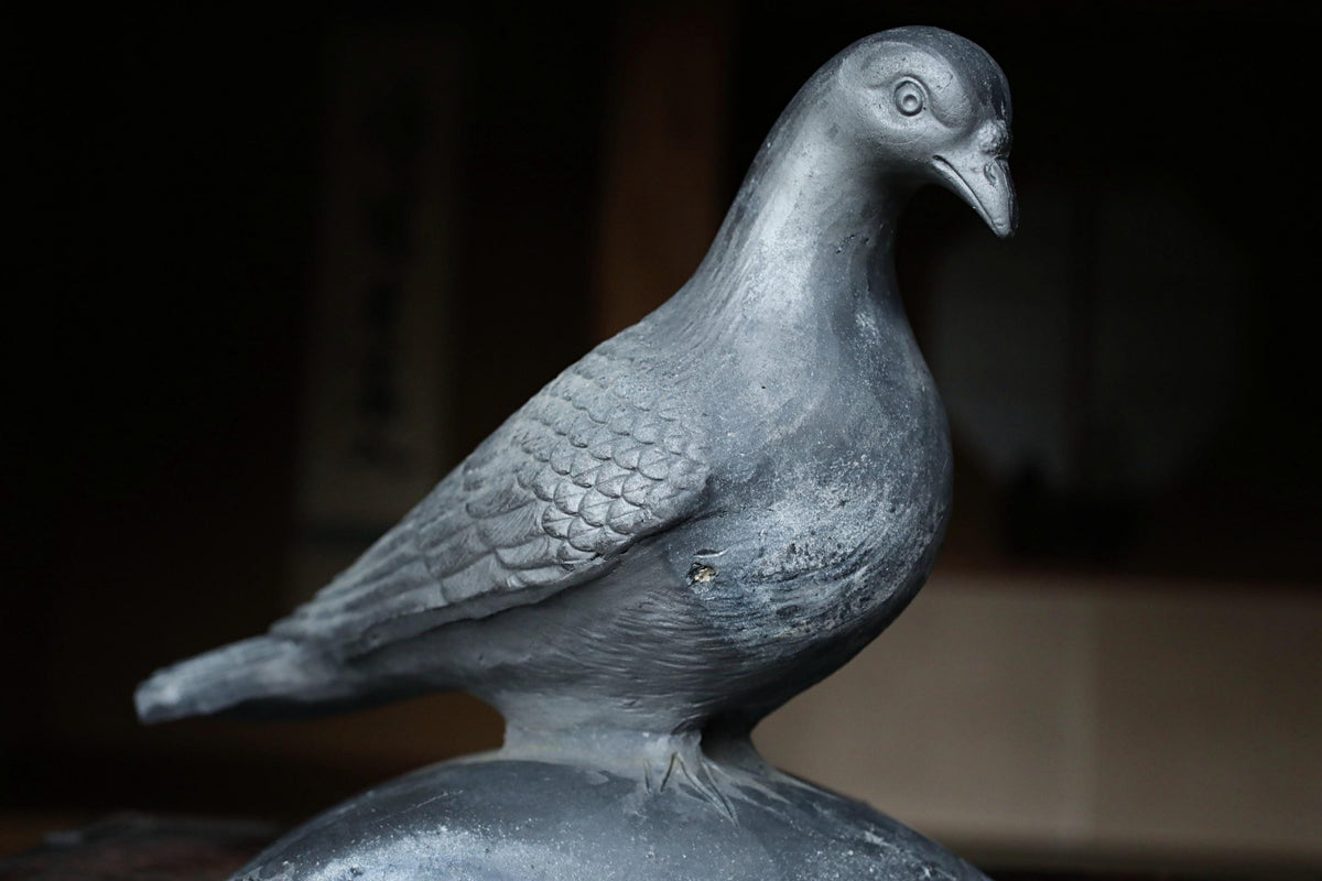 A close-up view of a metal bird statue, possibly a dove, perched on a surface.