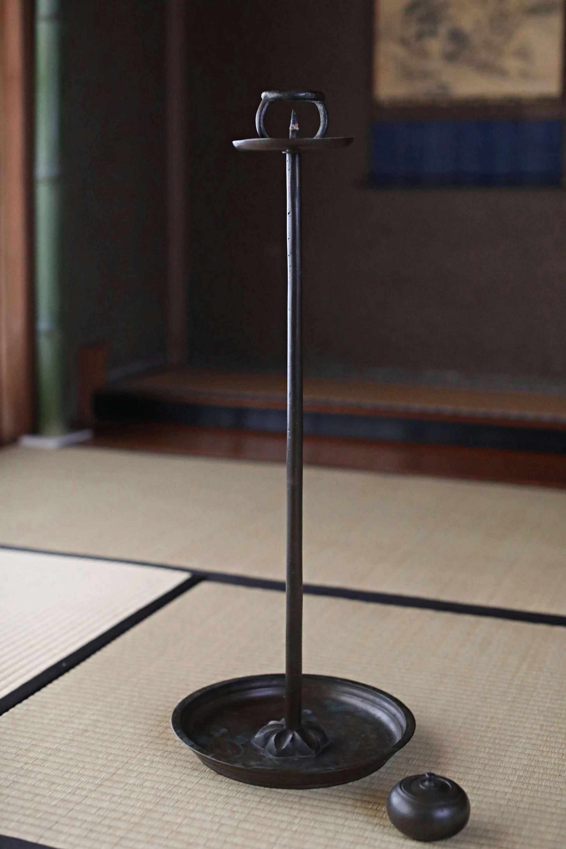 A black metal candlestick holder with a candle in the bottom right corner, placed on a woven mat.