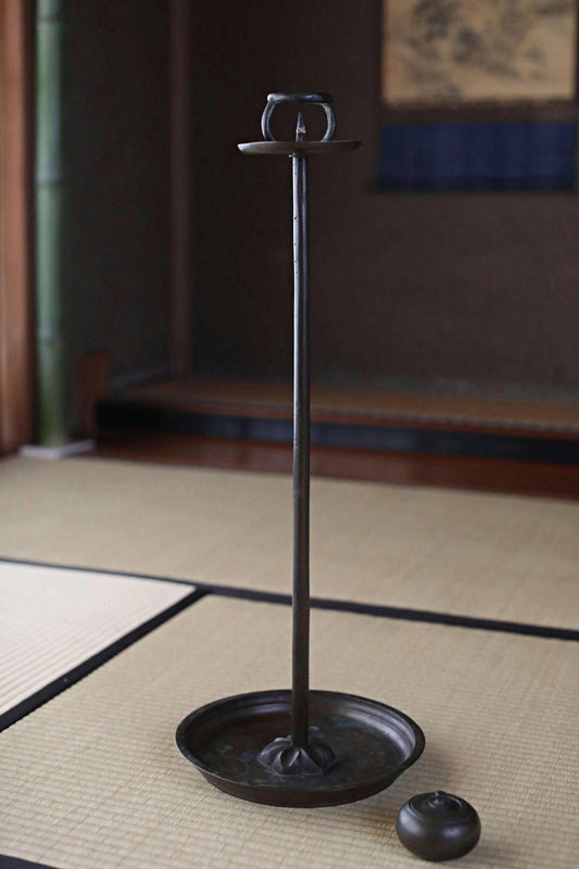 A black metal candlestick holder with a candle in the bottom right corner, placed on a woven mat.