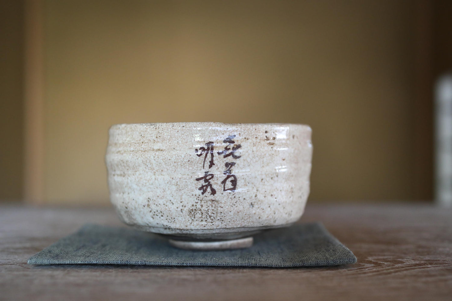 A white ceramic bowl with Chinese characters on it, placed on a gray cloth on a wooden surface.