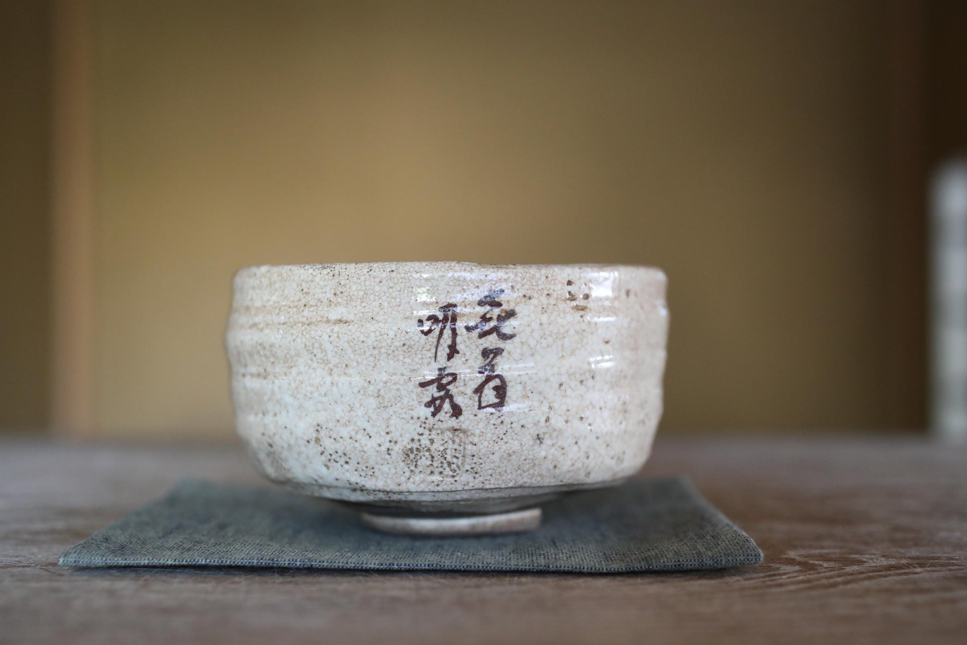 A white ceramic bowl with Chinese characters on it, placed on a gray cloth on a wooden surface.