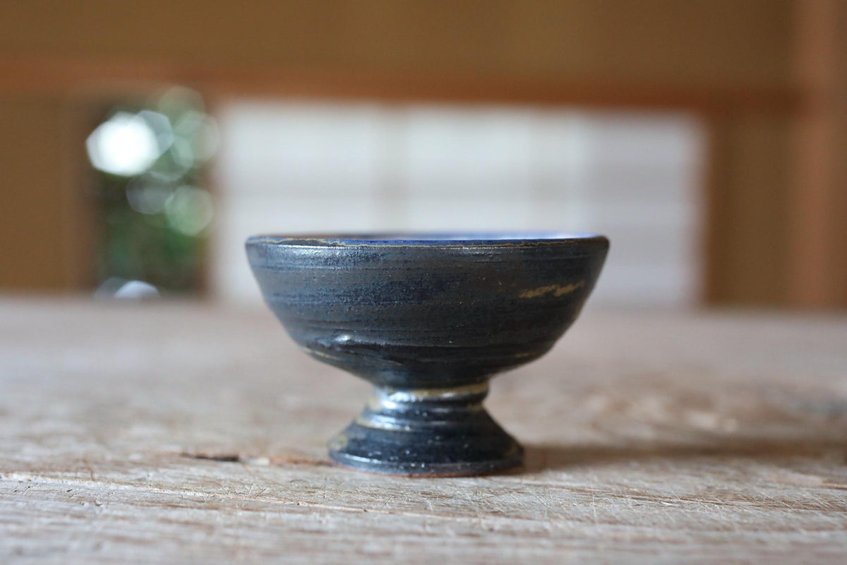 A small, black bowl sits on a wooden surface, with a blurred background suggesting an indoor setting.