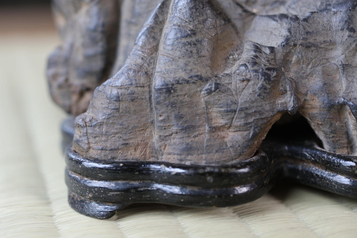 A close-up image of a wooden sculpture with a textured surface, resting on a woven mat or mat-like material.