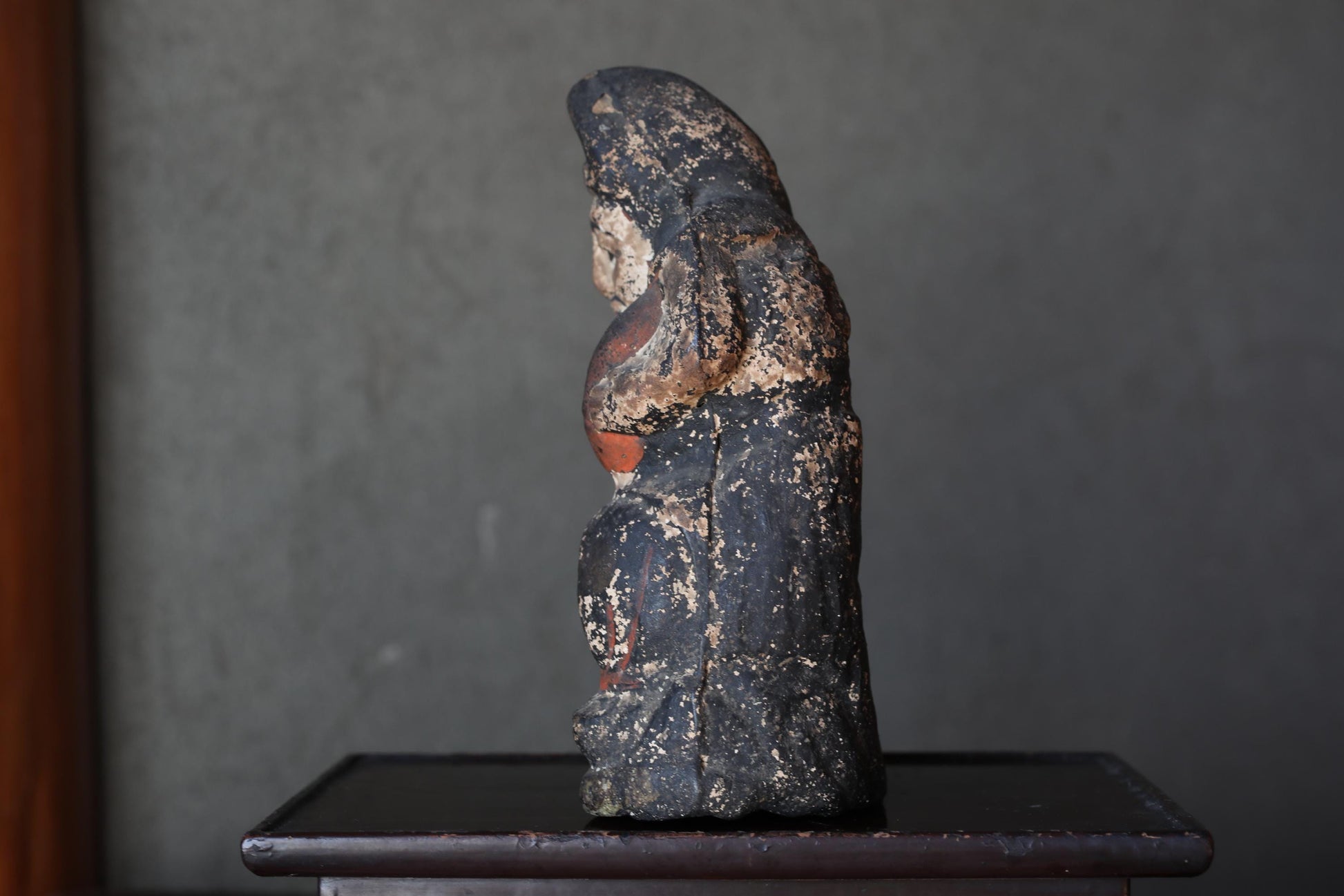 An old, weathered statue of a person sitting on a wooden surface.