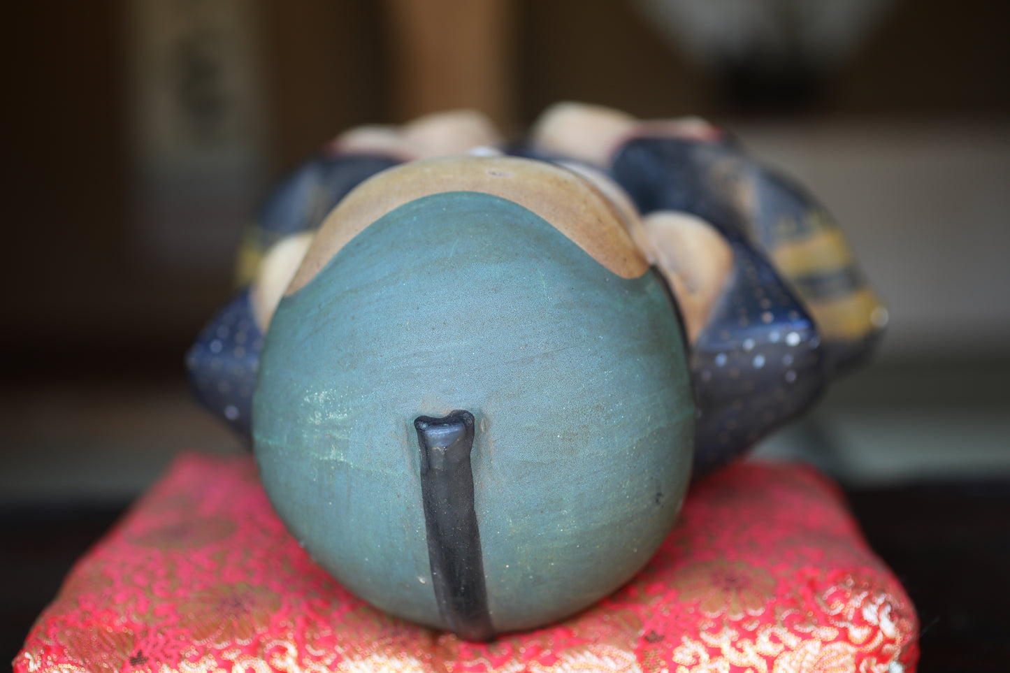 A close-up view of a ceramic figurine with a blue and black color scheme, resting on a red and orange patterned surface.