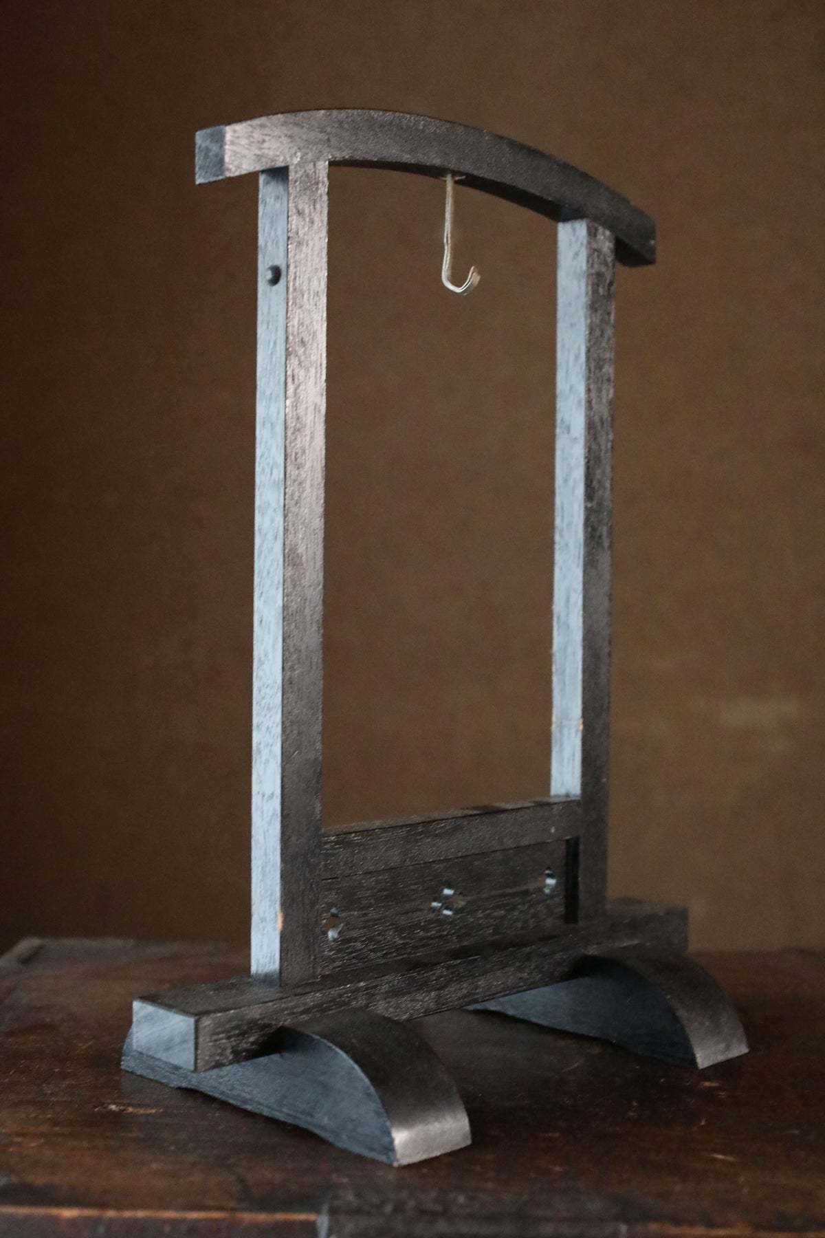 a wooden frame with a hook hanging from it, placed on a wooden surface.