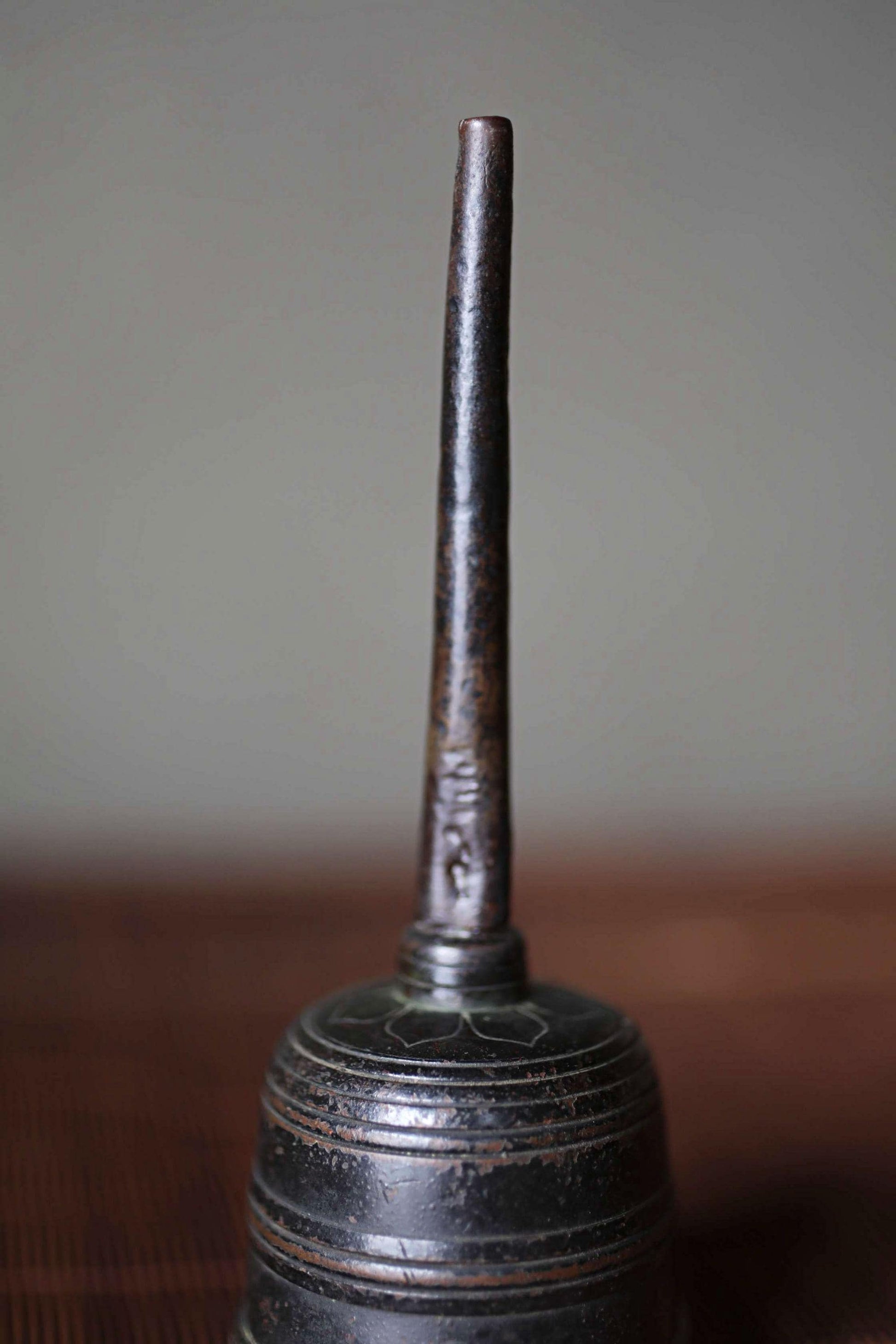 A close-up image of a metal object with a pointed end, possibly a tool or container, sitting on a wooden surface.